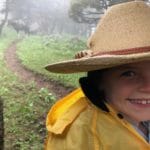 A little girl wearing a cowboy hat smiles amid a Montana rain storm.