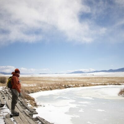 An angler stands over a frozen creek.