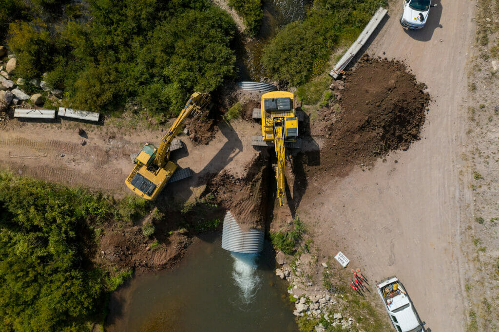Areal view of two excavators moving dirt for river tunnel under road