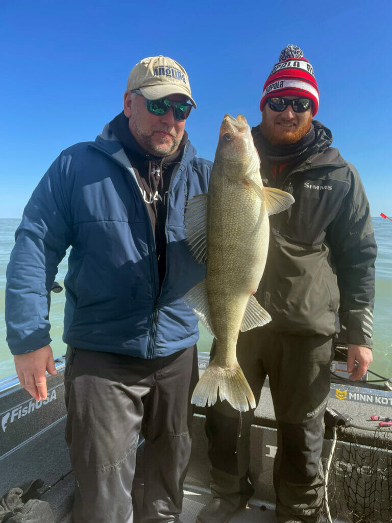 Two men standing in boat with a walleye