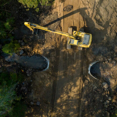 Backhoe next to a culvert on a dirt road