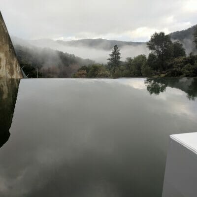 Smooth, still water next to damn with misty mountains in background