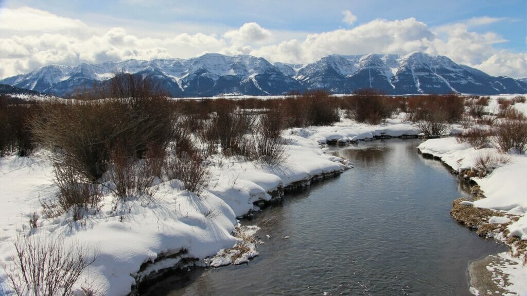 Clouds, snow capped mountains, snowy stream in Red Rocks Lakes Wildlife Refuge