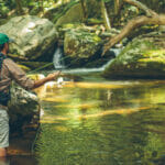 Man with backpack fly fishing in river