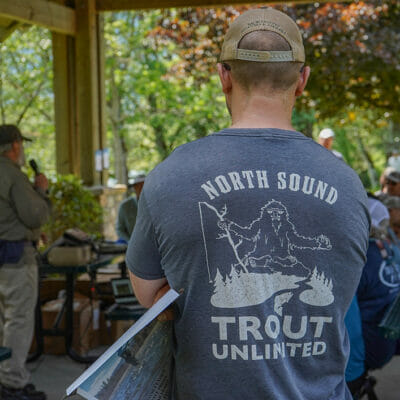 Man at gathering who's shirt reads "North Sound Trout Unlimited" and shows a sasquatch
