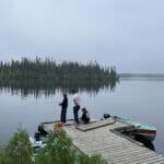 Three young men fishing from a dock with a big, beautiful, calm lake in the background