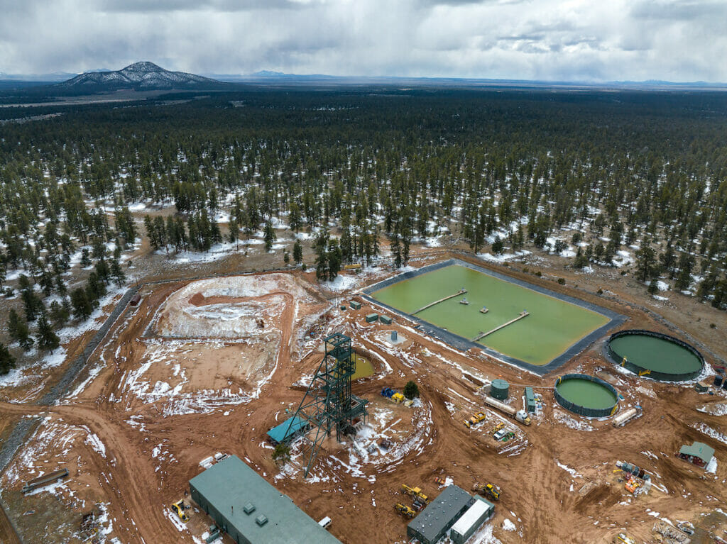 Overhead shot of area with torn up ground, machinery, water, surrounded by forrest.