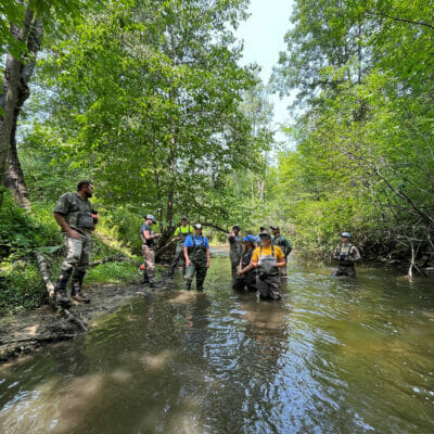 Group of people wearing waders stands in a stream